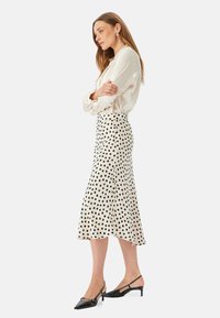 Polka dot midi nederdel i creme med sorte prikker, glat stof, flared design og høj talje. Parret med en lys bluse og sorte hæle.