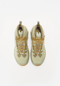 Adidași înalți cu un suprafață din suede de culoare verde deschis, accente bej, șireturi texturate și o talpă din cauciuc. Dispune de un guler și o limbă căptușite.