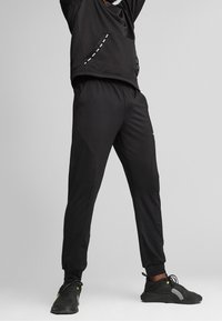 Svart sportig outfit bestående av en långärmad topp med en framficka och sömnadsdetaljer, matchad med tajta byxor. Tillverkad av ett smidigt material.