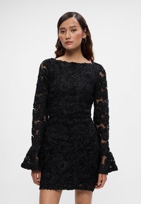 Melnas kleitas ar gariem, caurspīdīgiem piedurknēm, kas rotātas ar sarežģītu ziedu izšuvumu, pieguļoša apakšdaļa un izplešanās piedurknes. Materiāls ar teksturētu detaļu visā kleitā.