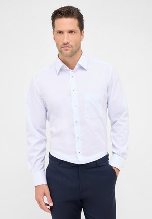 Chemise à carreaux blanche et bleu clair, à boutons, avec une poche unique, manches longues et tissu lisse. Portée avec un pantalon sombre.
