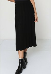 Jupe noire jusqu'au genou avec une texture côtelée, un design évasé et une taille ajustée. Assortie à des bottines noires à talon carré.