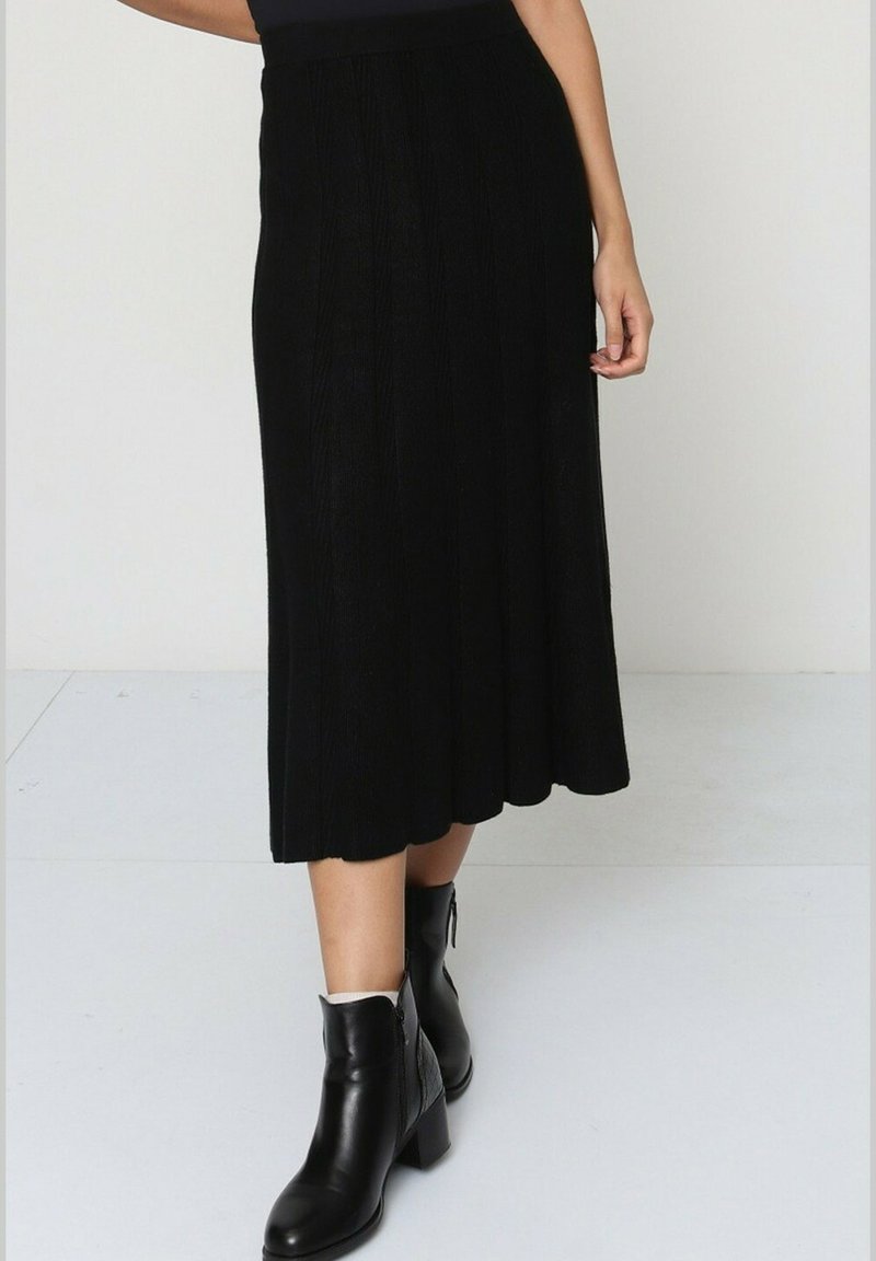 Jupe noire jusqu'au genou avec une texture côtelée, un design évasé et une taille ajustée. Assortie à des bottines noires à talon carré.