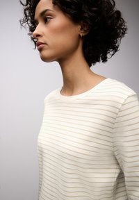 Leichter, strukturierter Pullover mit cremefarbenen und beigen Streifen, Rundhalsausschnitt und langen Ärmeln, gezeigt im Seitenprofil eines Models.