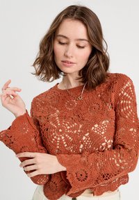Hæklet sweater i rustfarve med indviklede blomsterdesigns, lange flagrende ærmer, en løs pasform og en rund halsudskæring.