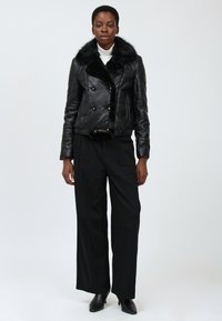 Veste noire en cuir à double boutonnage avec un col en fausse fourrure, ornée de boutons dorés, au design court associée à un pantalon noir à large jambe.