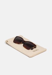 Ochelari de soare cu ramă din țestoasă, cu lentile întunecate, așezați pe un pouch bej. Pouch-ul are branding aurie "LIU•JO" și sistem de închidere cu șiret.