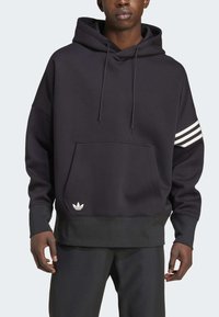 Sudadera negra hecha de tejido suave, con un bolsillo frontal, capucha con cordón y tres franjas blancas en la manga izquierda. Logo en el dobladillo.