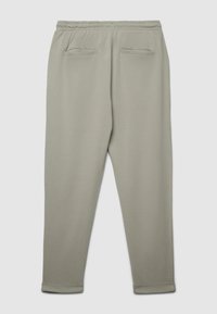 Pantaloni della tuta grigio chiaro realizzati in tessuto morbido, con cintura elastica, due tasche posteriori e polsini sagomati alle caviglie.