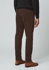 Pantalones de pana marrones con corte recto, tejido texturizado y detalle en el bolsillo trasero. Combinados con botas de tobillo de ante marrones.