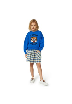 Blauer Sweatshirt mit einem orangen Tiger-Graphic und dem Text "KENZO PARIS". Kombiniert mit einem grün-blauen karierten Rock und weißen Sneakers.