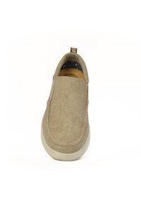 Zapato beige de tipo slip-on, hecho de una tela texturizada, con punta redondeada y suela ligera. El interior presenta un forro azul con un diseño.