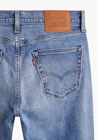 Jean en denim bleu clair avec grande poche arrière et écusson en cuir marron Levi Strauss au-dessus de la poche sur la ceinture.