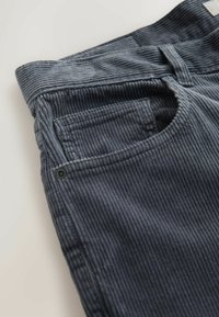 Gray corduroy fabric with vertical ribs, featuring a front pocket and a buttonhole detail. The waistband has a smooth finish.