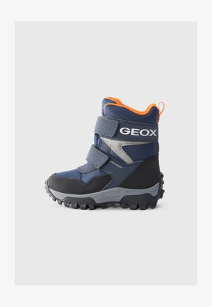 Bota de invierno en azul marino y negro con dos correas ajustables de Velcro en gris, detalles en naranja, suela resistente y diseño impermeable.