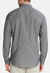 Camicia button-up grigia con un motivo geometrico bianco, maniche lunghe e orlo curvo. Presenta un colletto e polsini con bottoni.