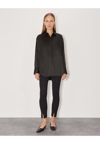 Camicia nera di raso a maniche lunghe con colletto, abbinata a leggings neri sartoriali con spacchi laterali e scarpe basse nere.