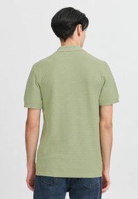 Kortermet, lysegrønn polo-skjorte med en strukturert strikkemønster. Har krage og rett kant. Brukt med mørke jeans.