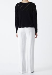 Czarny sweter dziany z diagonalnymi nacięciami, noszony na białych, szerokich spodniach. Gładka tekstura, luźny krój i okrągły dekolt.