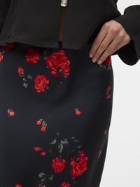 Black top with a button detail paired with a fitted skirt featuring red rose patterns against a black background. Smooth fabric texture.