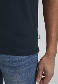 Mørkeblå bomulds T-shirt med rund halsudskæring og korte ærmer. Har et lille stofmærke i kanten. Kombineret med lys blå denimjeans.