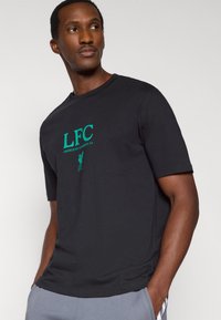 Czarny bawełniany t-shirt z zielonym logo "LFC" i napisem na środku klatki piersiowej, krótkie rękawy oraz klasyczny okrągły dekolt.