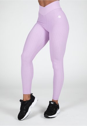 Lavendel hoge taille legging met een gestructureerd, golfpatroon. Gecombineerd met zwarte sportsneakers met witte zolen en accenten.
