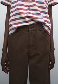 Pantaloni in cotone marrone con tasche frontali, abbinati a una maglietta a righe multicolori con strisce rosse, blu e panna e maniche corte.