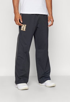 Dunkelgraue Sporthose aus leichtem Material, mit einem subtilen Glanz, seitlichen Streifen und einem gestickten Logo auf dem linken Oberschenkel.