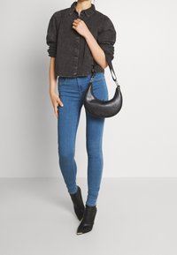 Czarna koszula z denimu na guziki z bufkami, zestawiona z dopasowanymi niebieskimi dżinsami i małą czarną skórzaną torebką w kształcie półksiężyca. Czarne, szpiczaste botki za kostkę.