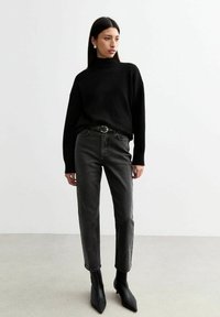 Svart stickad polotröja, högmidjade kolgrå jeans och svarta spetsiga ankelboots. Minimalistisk design med en ren silhuett.