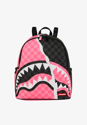 Mochila con patrón de tablero de ajedrez dividido en rosa y negro, que presenta una gran boca de tiburón estilizada con afilados dientes blancos en la parte frontal.
