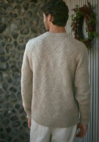 Jasno beżowy sweter dzianinowy z teksturowanym wzorem w jodełkę, okrągłym dekoltem oraz ściągaczami przy mankietach i hemie.