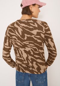 Braun- und beigefarbener Tigerstreifen-Pullover aus weichem Strickmaterial, mit langen Ärmeln und rundem Halsausschnitt, kombiniert mit blauen Jeans.