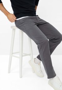 Chinos grigi in cotone con vestibilità dritta, dotati di tasche anteriori e una texture morbida, abbinati a sneaker bianche e un maglione scuro.