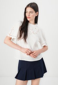 Biely ľanový blouse s kvetinovým vyšívaním na rukávoch a výstrihu, kombinovaný s námornícky plisovanou sukňou. Ľahká, textúrovaná látka.