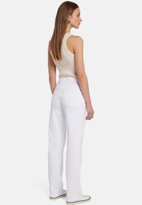 Pantaloni bianchi a gamba larga con vita alta e due tasche posteriori, abbinati a un top aderente beige a costine. Tessuto dalla texture liscia.