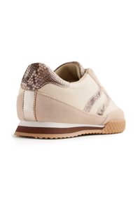 Sneaker beige con un accent di pelle di serpente testurizzata al tallone, tomaia in suede, suola bianca e marrone e strisce marroni a contrasto.