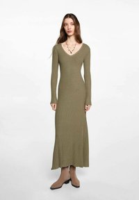 Abito a coste verde oliva con scollo a V, maniche lunghe e lunghezza maxi, abbinato a stivali alla caviglia beige.