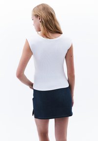 Weißes geripptes ärmelloses Oberteil mit rundem Ausschnitt, kombiniert mit einem dunklen Jeans-Minirock mit seitlichen Reißverschlüssen und Kontrastnähten.