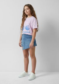 Helles rosa T-Shirt mit blauer Kirschgrafik und dem Text "CHERRYLICIOUS", kombiniert mit einem Jeansrock und weißen Turnschuhen.