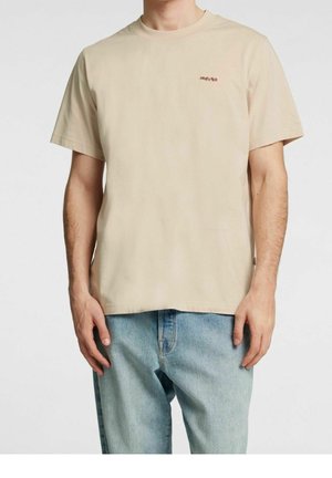 Beżowy T-shirt z krótkim rękawem wykonany z bawełny, z małym czerwonym logo na piersi. W połączeniu z jasnoniebieskimi dżinsami.