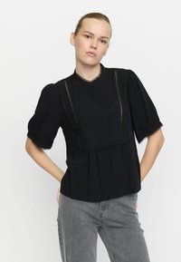Schwarze Bluse mit kurzen, gepufften Ärmeln, plissiertem Vorderteil und Spitzenrandakzenten. Verfügt über einen knöpfbaren Hals und eine lockere Passform.