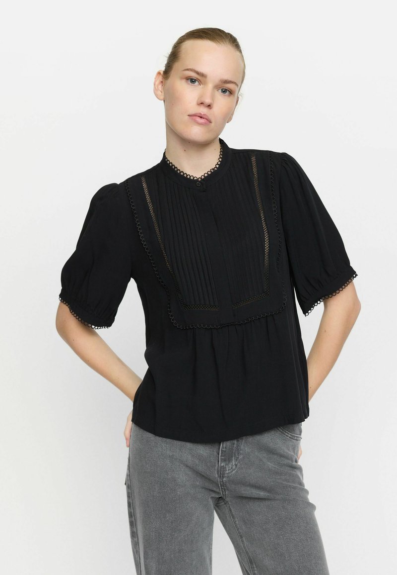 Schwarze Bluse mit kurzen, gepufften Ärmeln, plissiertem Vorderteil und Spitzenrandakzenten. Verfügt über einen knöpfbaren Hals und eine lockere Passform.
