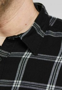 Camicia a quadri nera con un motivo a scacchi e accenti bianchi e grigi. Presenta un colletto a punta e un tessuto testurizzato.