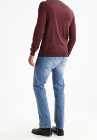 Bordeaux gestrickter Pullover, schlanker Schnitt, weiche Textur; kombiniert mit hellblauen Jeans, leicht ausgebleicht, und schwarzen Stiefeletten.