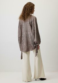 Bluza cu maneci lungi, de culoare taupe, cu un model floral, realizată dintr-un material lucios. Asortată cu pantaloni evazați, de culoare crem, cu margini destramate și tocuri negre.