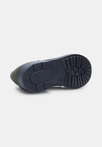 Talpa de pantof cu cauciuc de culoare bleumarin închis, texturată pentru aderență, având un model de profil și o margine rotunjită. Partea superioară din suede verde se întâlnește cu talpa.