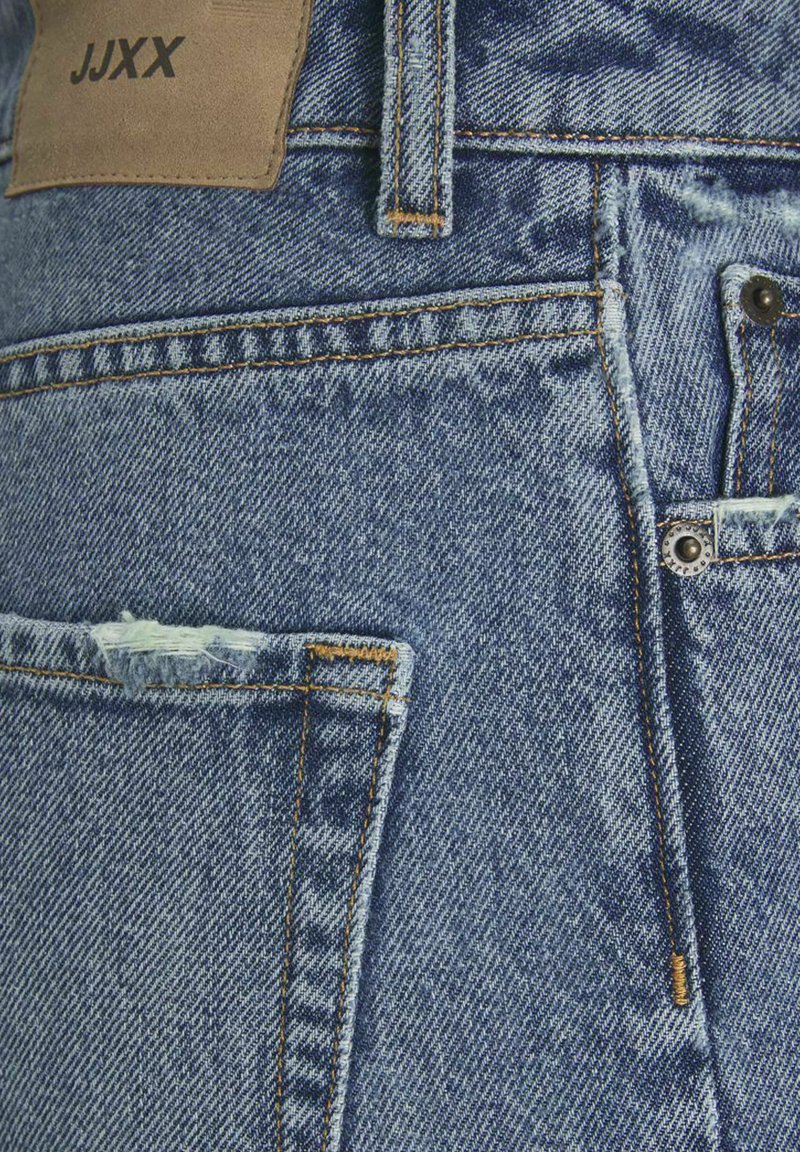 Jeans in denim blu presentano una toppa in pelle beige, molteplici tasche, cuciture arancioni a contrasto e un accento invecchiato sulla tasca anteriore.