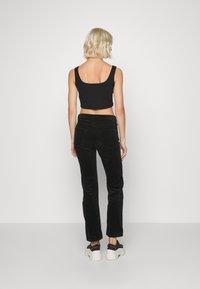 Zwarte flanellen flare broek met achterzakken, gecombineerd met een strakke zwarte crop top. Model draagt zwarte chunky sneakers.